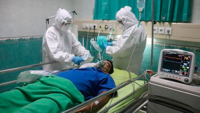 A imagem mostra dois médicos usando roupa completa de proteção contra doenças transmissíveis cuidando de um paciente.