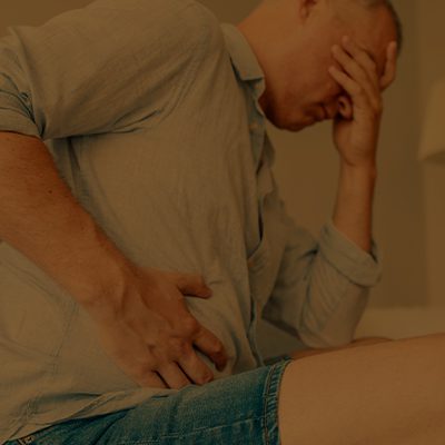 A imagem mostra um homem com dor com a mão na região do estômago.
