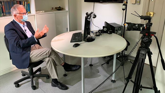 A imagem mostra o Prof. Dr. Luiz Carneiro gesticulando com as mãos, na frente de um computador.