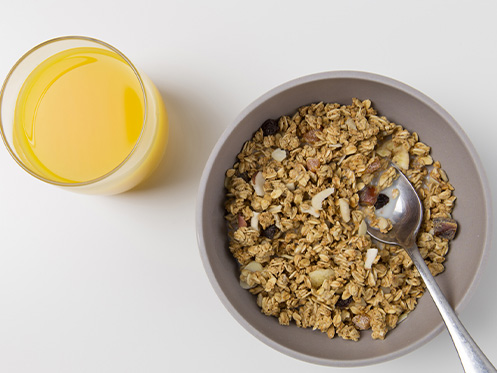 Imagem ilustra um pote de granola ao lado de um suco de laranja.