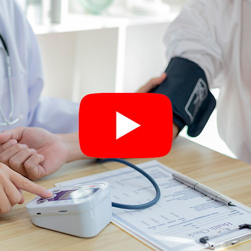Médico aferindo a pressão arterial de um paciente em consultório, com estetoscópio e equipamentos médicos sobre a mesa.
