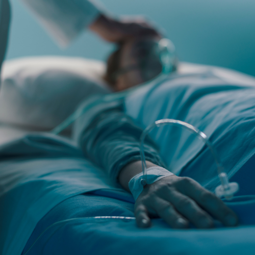 Paciente hospitalizado em leito, com acesso venoso e oxigênio, recebendo cuidados médicos em ambiente clínico.