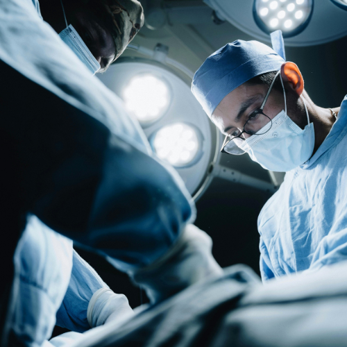 Equipe cirúrgica realizando procedimento em centro cirúrgico, sob luzes operatórias, com profissionais paramentados e focados na cirurgia.
