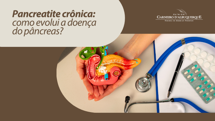 Modelo anatômico do sistema digestivo e pâncreas segurado pelas mãos, ao lado de estetoscópio sobre mesa médica.