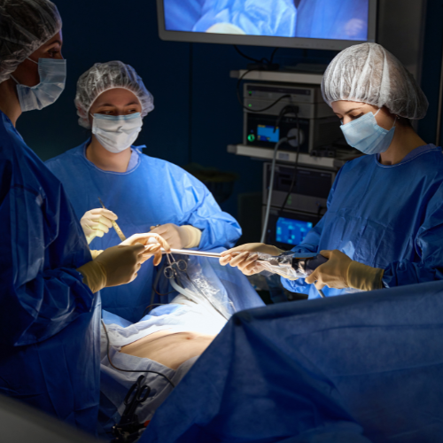 Equipe médica realiza procedimento cirúrgico em centro cirúrgico com equipamentos e monitoramento ao fundo.