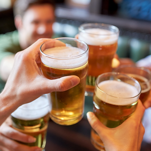 Pessoas brindando com copos de cerveja, representando o consumo de álcool e seus impactos na saúde do fígado.