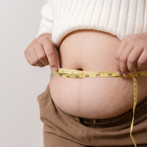 Pessoa medindo a circunferência abdominal com fita métrica, destacando aumento do abdômen.